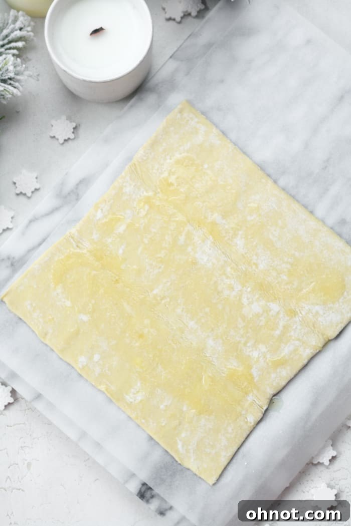 Unrolled puff pastry dough laid out flat on a marble surface, ready for seasoning.