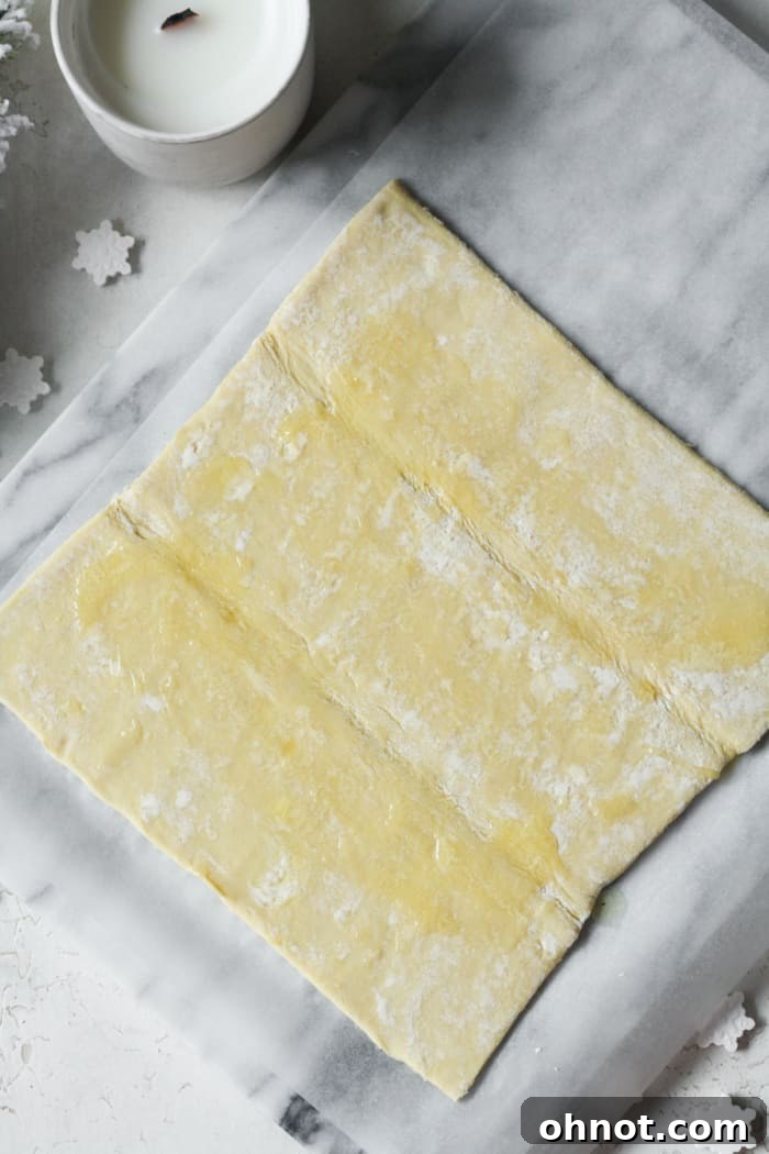 Puff pastry sheet brushed with melted butter on a marble block, preparing for the next layer.