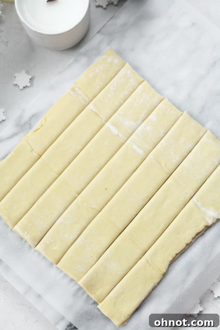 Layered puff pastry dough expertly sliced into uniform 1-inch strips using a pizza cutter.