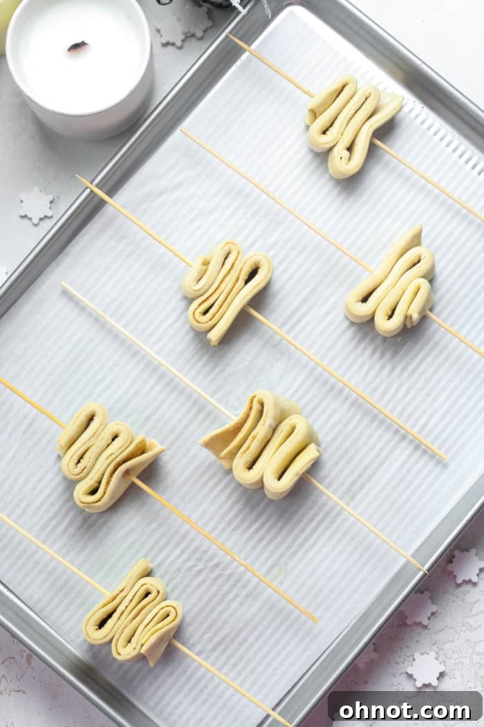 Small, accordion-folded puff pastry trees, some with wooden skewers inserted, on a prepared baking sheet.