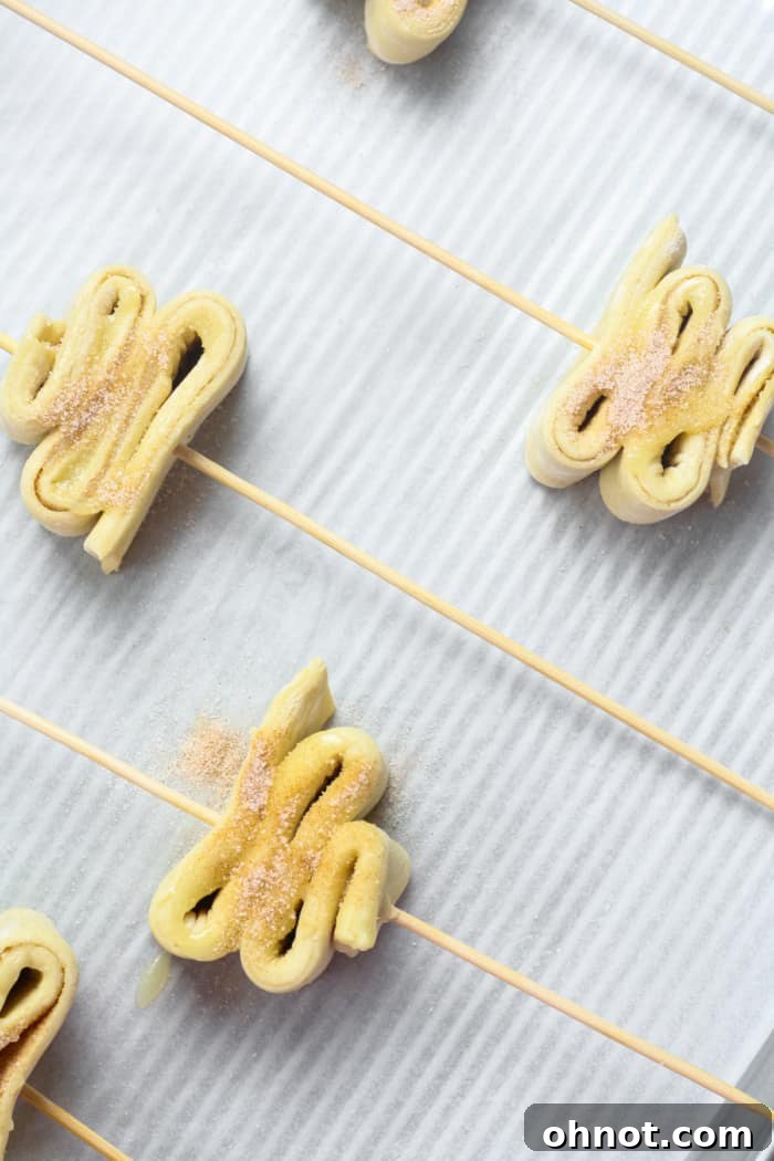 Accordion-folded puff pastry trees, each on a wooden skewer, neatly arranged on a baking sheet lined with parchment paper.