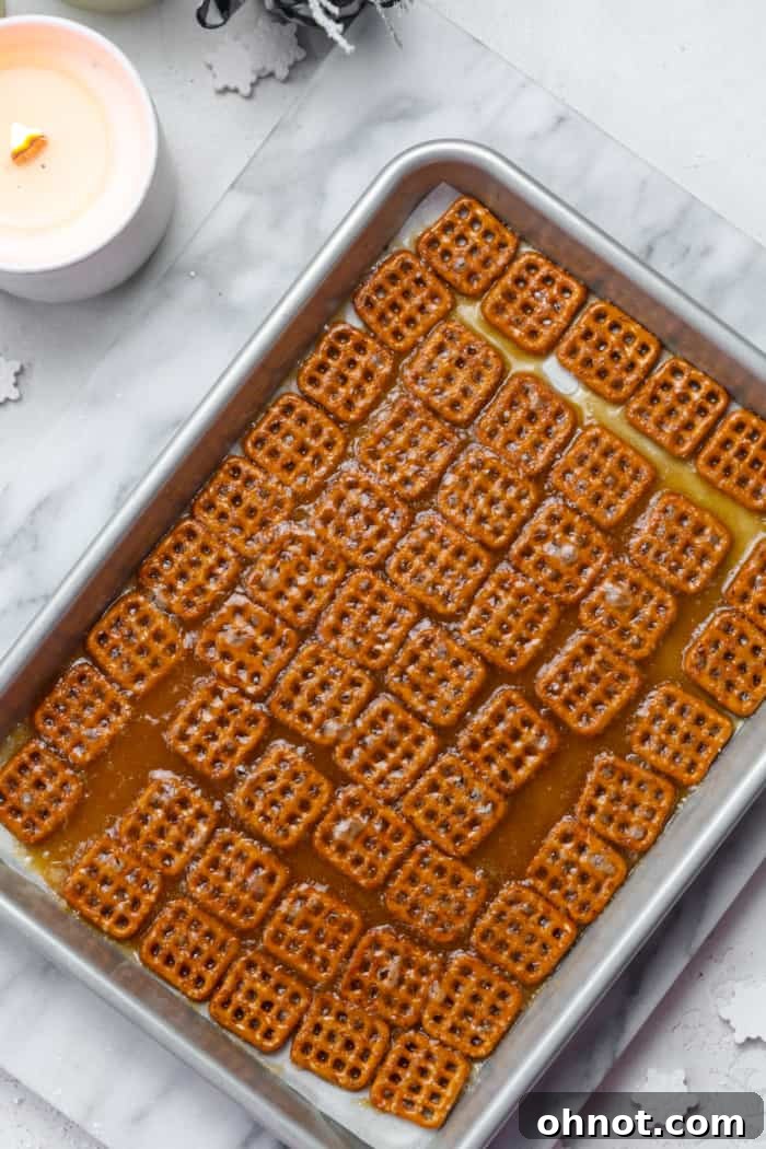 Hot caramel sauce freshly poured over a layer of pretzels on a baking sheet.
