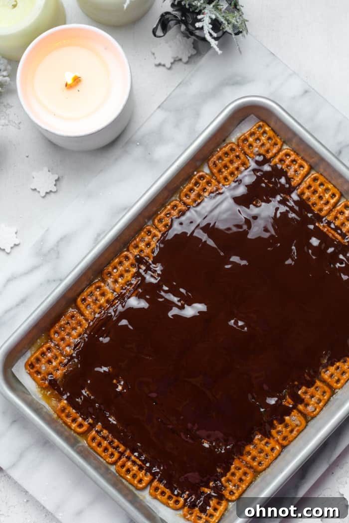 Melted chocolate freshly poured over the hot caramel-coated pretzels on a baking pan.