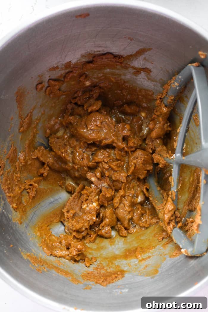 Wet orange-tinted cookie dough in a mixer bowl after adding egg and vanilla.
