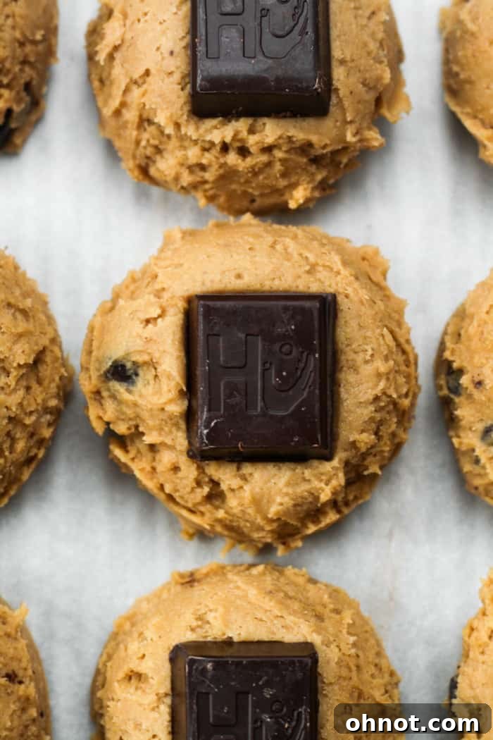 Raw cookie dough balls with a chocolate square pressed onto each, on a baking sheet.