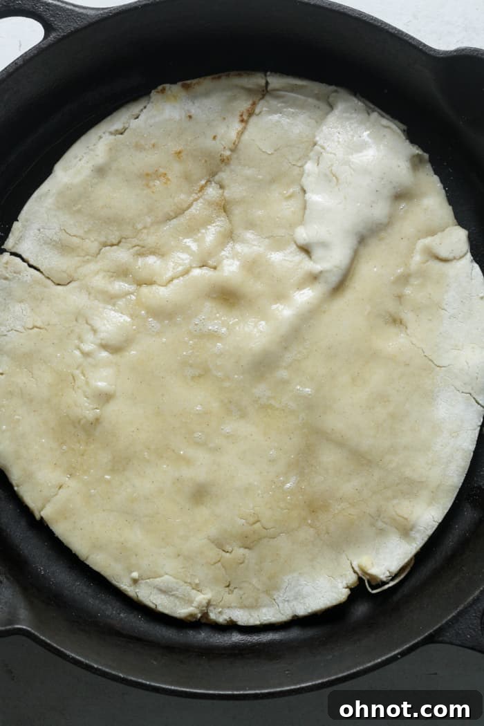 The pizza dough cooking in a black cast iron skillet on the stovetop, developing a golden-brown bottom.