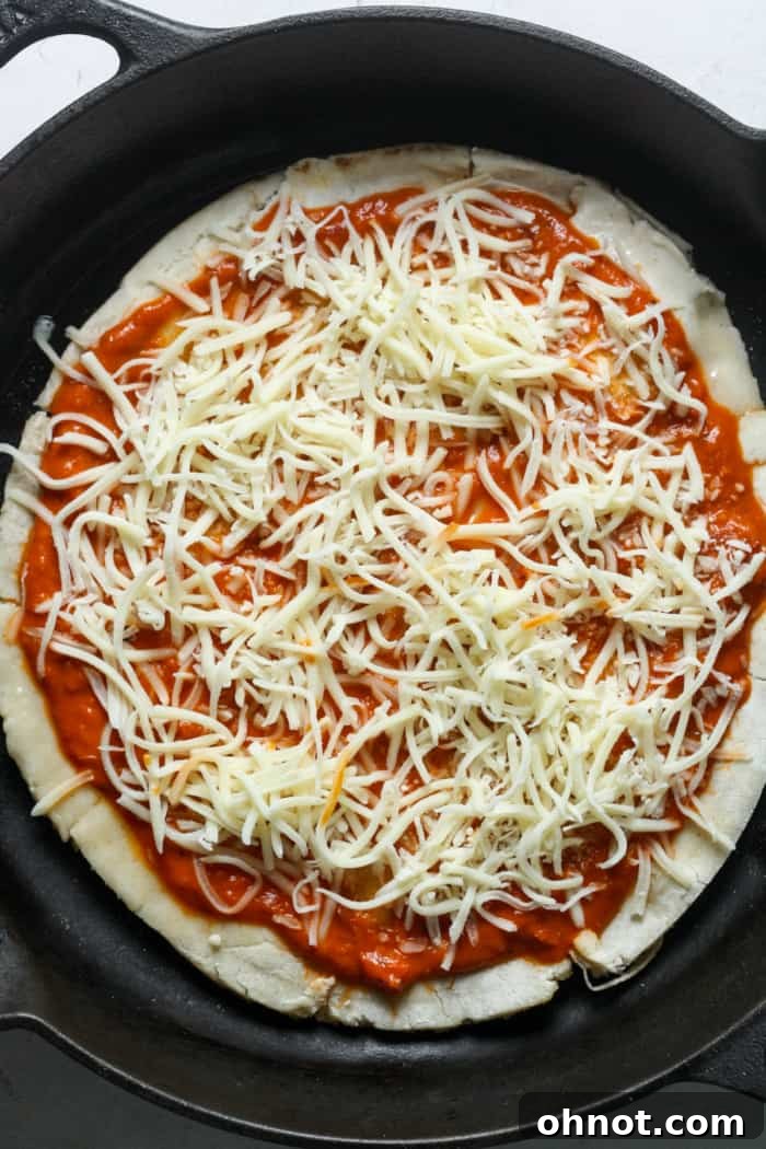 An unbaked pizza in a skillet, topped with sauce, cheese, and various ingredients, ready for the oven.