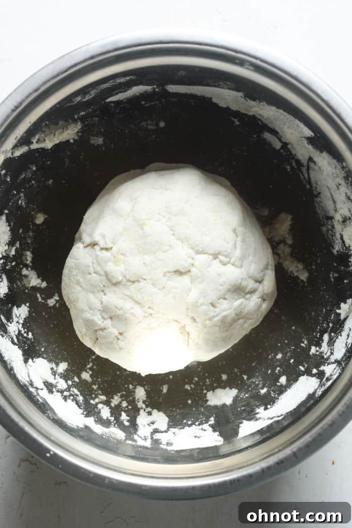 A perfectly formed ball of pizza dough resting in a mixing bowl, ready for fermentation.