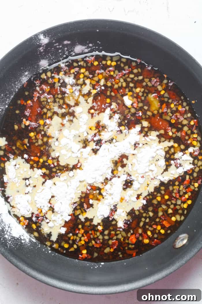 Whisking cornstarch into the simmering spicy sauce in a skillet to achieve desired thickness.