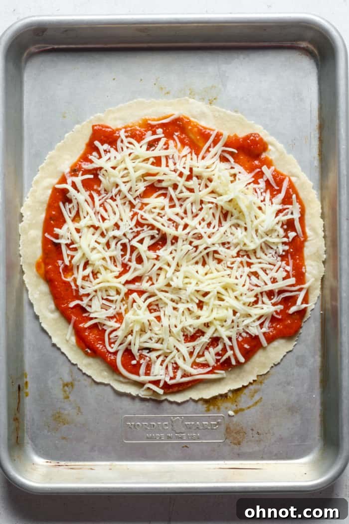 A tortilla generously topped with sauce, cheese, and various toppings on a baking sheet.