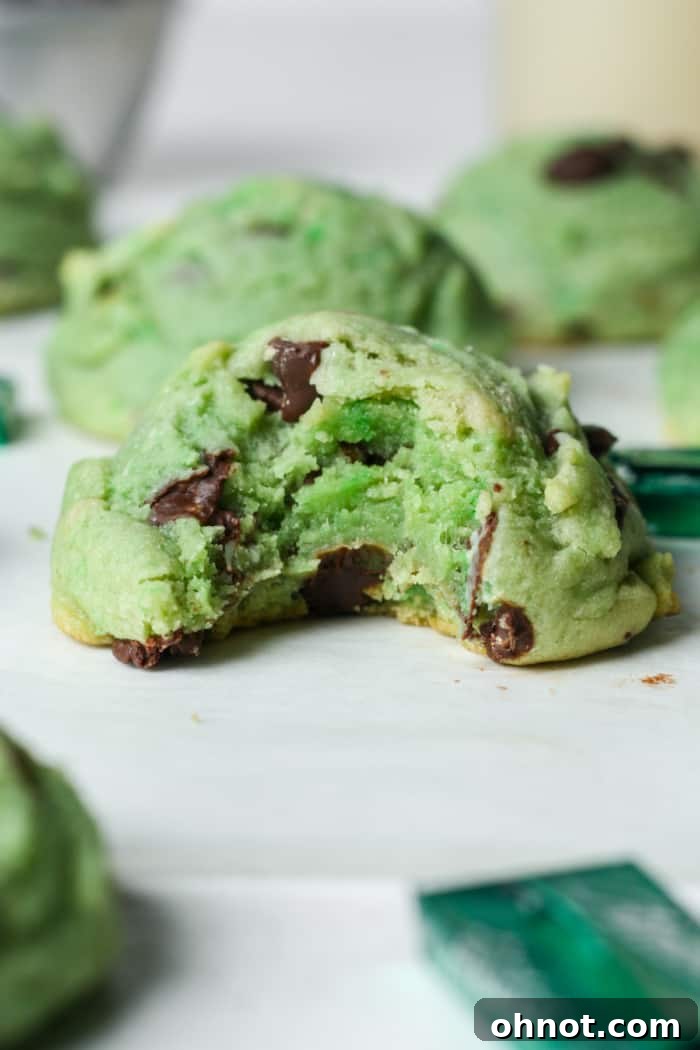 Close-up of a mint chocolate chip cookie with a bite taken out, showing the gooey center.