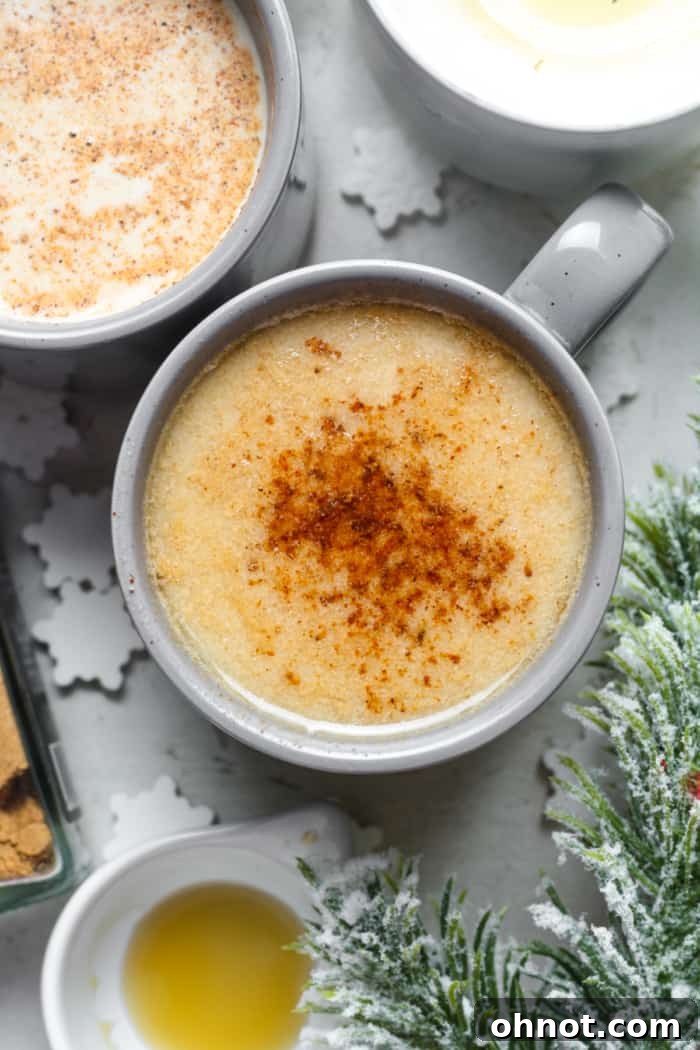 Rich and creamy vegan eggnog in a glass mug, garnished with a sprinkle of nutmeg, set against a festive background.