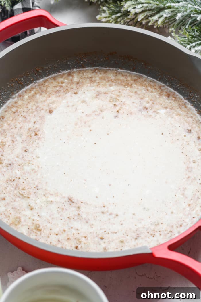 Vegan eggnog simmering gently in a pan on the stovetop, being stirred with a whisk.