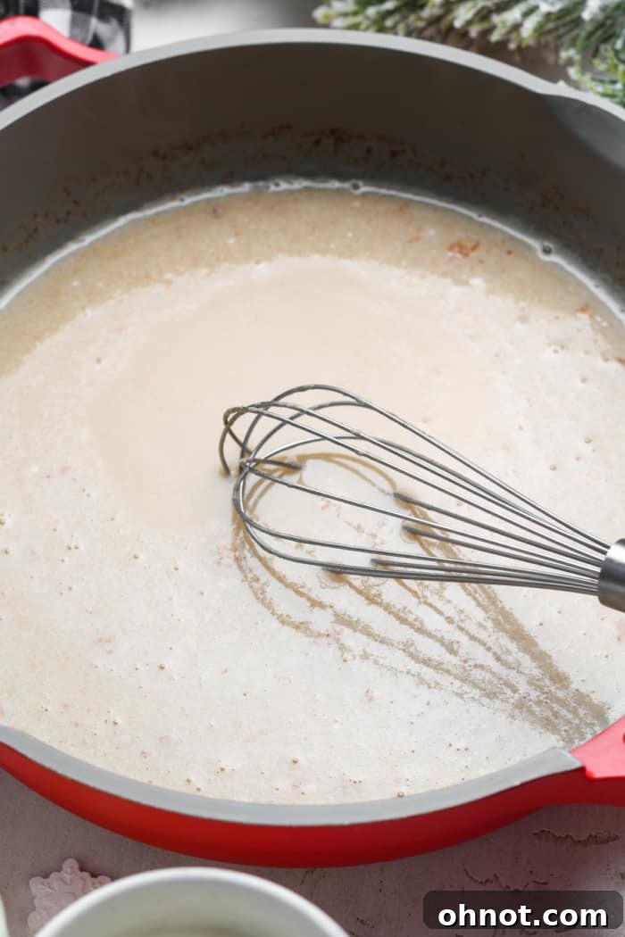 Close-up of a whisk stirring frothy and creamy vegan eggnog in a pan.