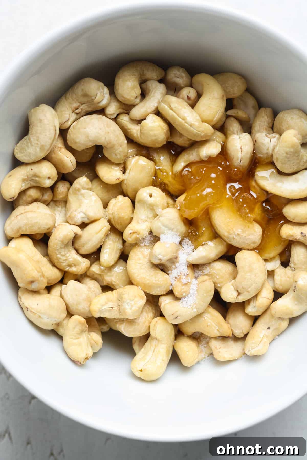 Raw cashews, honey, and melted butter being mixed in a bowl.