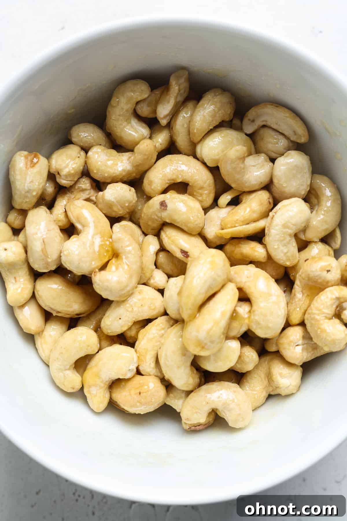 Cashews thoroughly coated with honey and butter, with sea salt sprinkled on top in a mixing bowl.