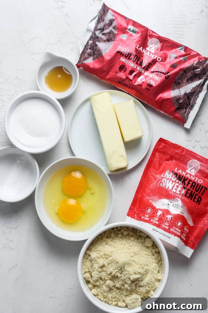 Assortment of ingredients laid out for making low carb cookies, including butter, monk fruit, eggs, almond flour, and sugar-free chocolate chips.