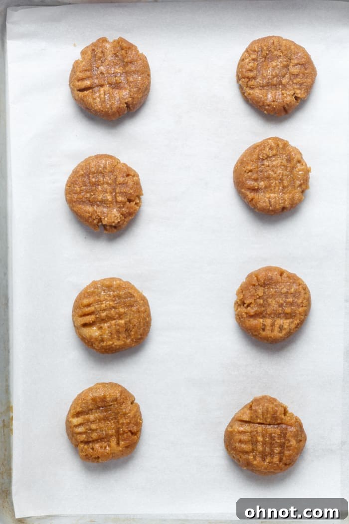 Raw keto peanut butter cookie dough balls with criss-cross fork marks on a baking sheet.