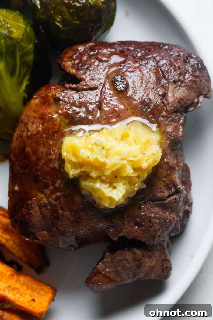Perfectly cooked filet mignon topped with a pat of melting compound butter and fresh herbs.