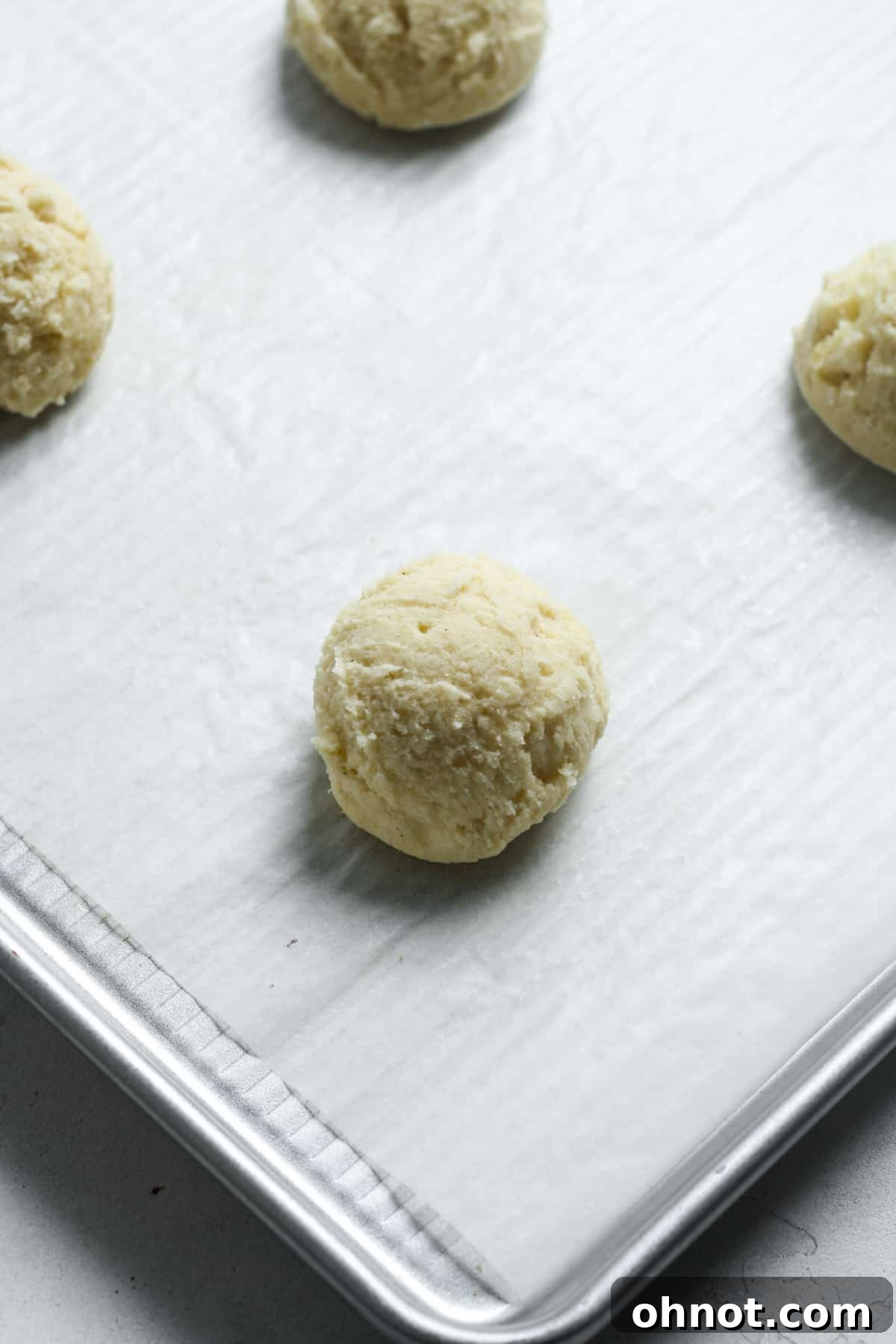 Balls of vegan cookie dough on a parchment-lined baking pan.