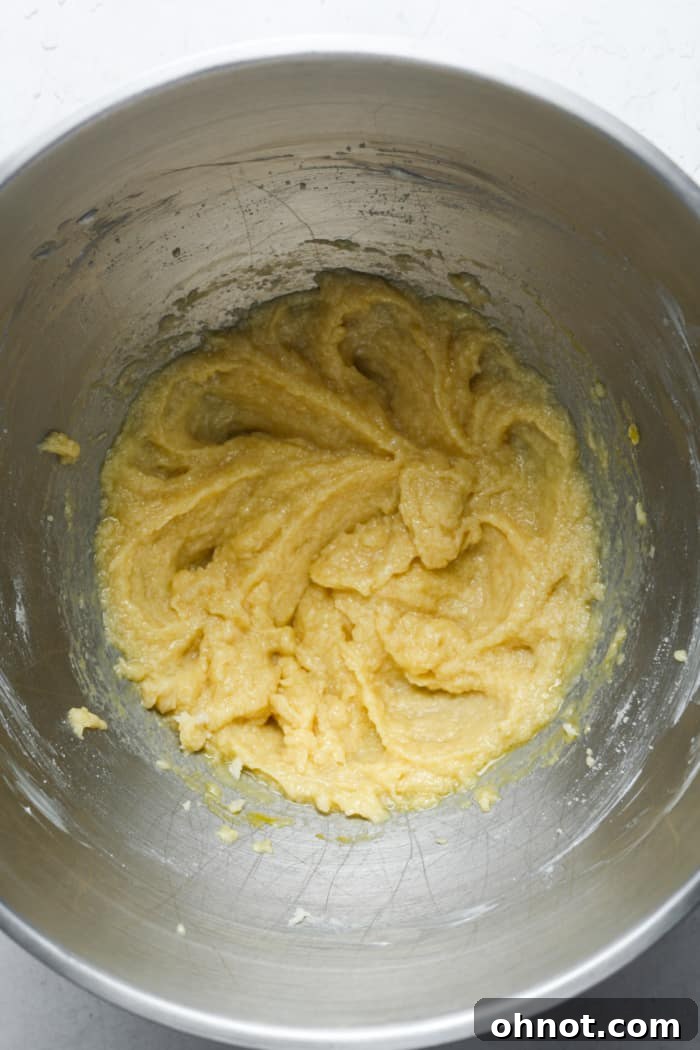 Pale yellow cookie dough in a mixing bowl after the egg and vanilla have been added, showing a smooth, creamy consistency.