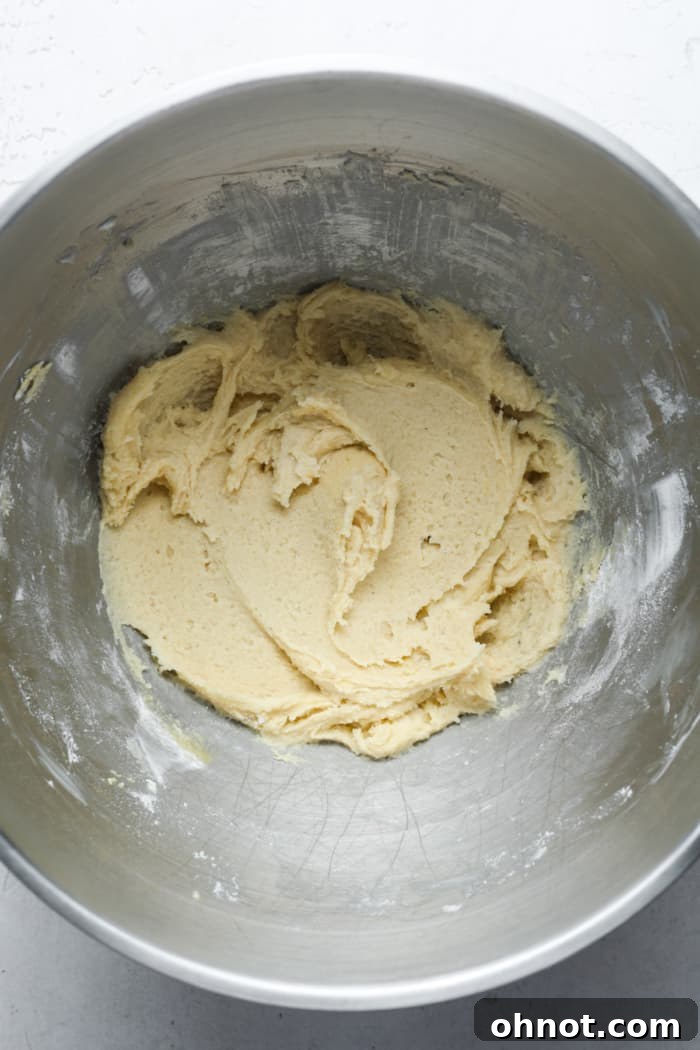 Thick, light-colored cookie dough in a mixing bowl after the dry ingredients have been added, ready for the final fold.