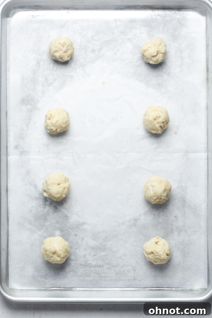 Evenly spaced balls of coconut cookie dough on a parchment-lined baking sheet, ready for baking.
