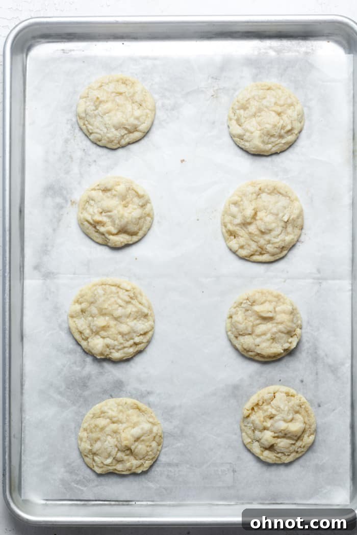 Freshly baked coconut cookies on a baking sheet, showing golden edges and soft centers, just out of the oven.