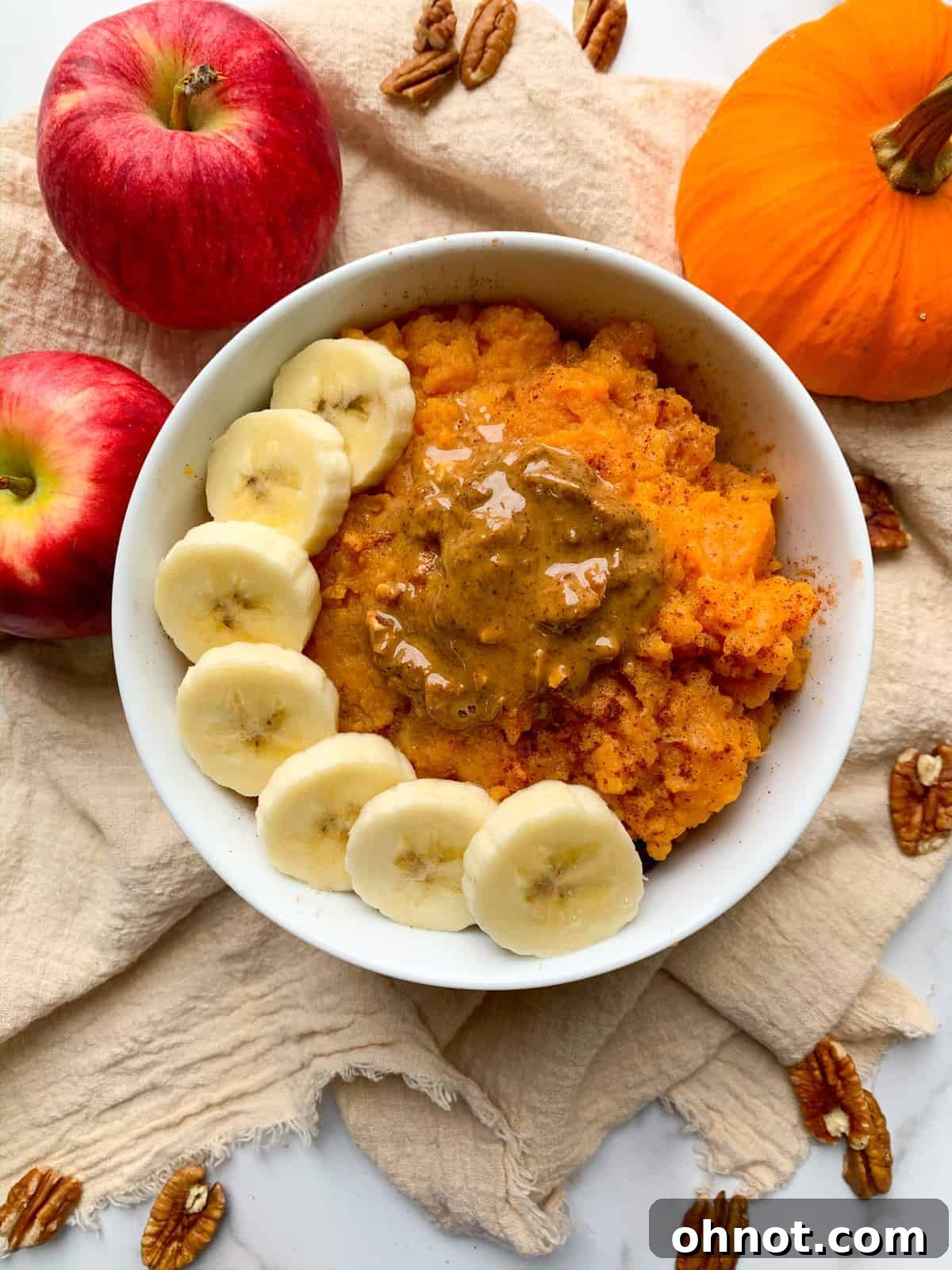 Warm and cozy sweet potato breakfast bowl topped with sliced banana and a drizzle of almond butter, sprinkled with cinnamon and nutmeg.