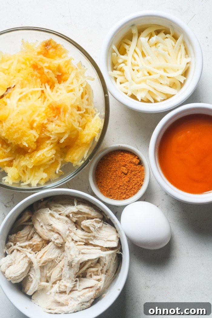 A vibrant selection of ingredients for buffalo chicken spaghetti squash, including buffalo sauce, spices, and shredded chicken in a bowl.