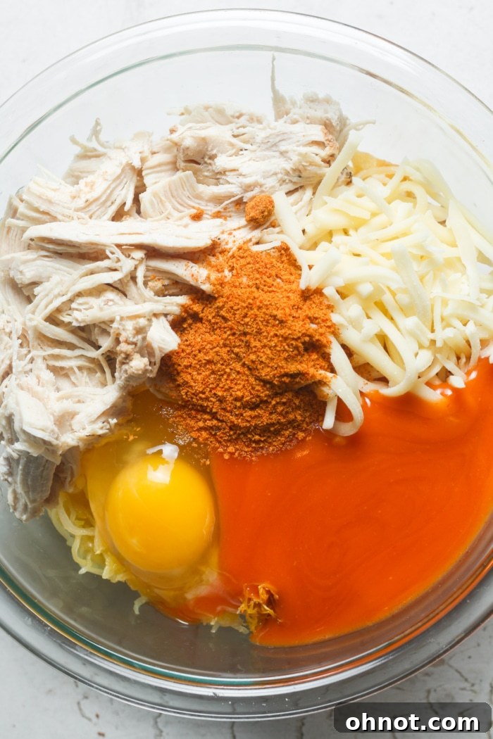 A large mixing bowl containing essential liquid ingredients like buffalo sauce, various spices, and a cracked egg, poised for blending with other components.