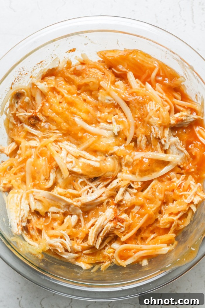 A close-up view of the perfectly combined, cheesy, creamy buffalo chicken and spaghetti squash mixture in a large mixing bowl.