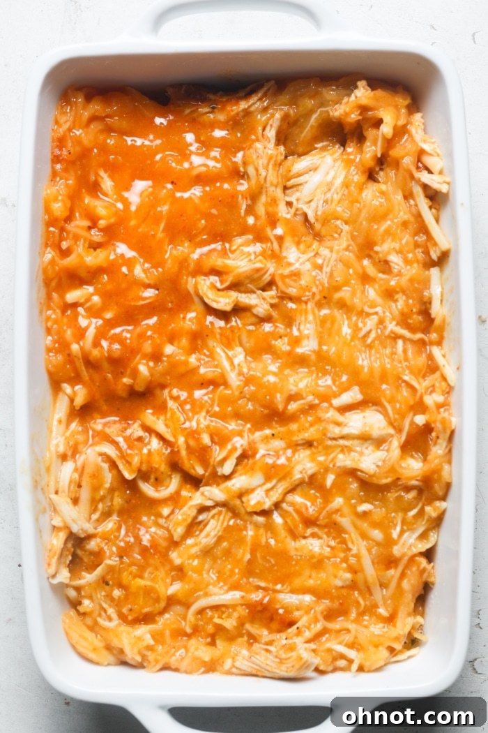 The orange-hued buffalo chicken spaghetti squash mixture neatly and evenly transferred into a baking dish, poised for baking in the oven.
