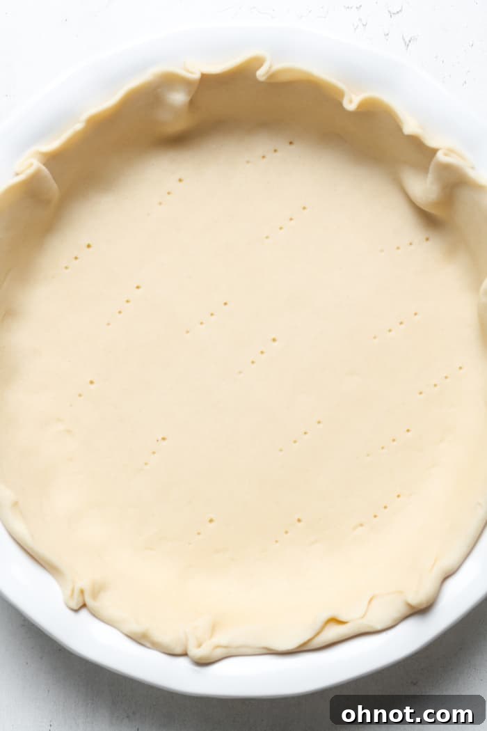 Unbaked pie crust, neatly crimped and pierced with a fork, resting in a pie plate, ready for blind baking.