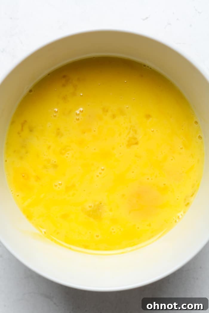 Five eggs, freshly whisked until light and airy, in a large glass bowl.