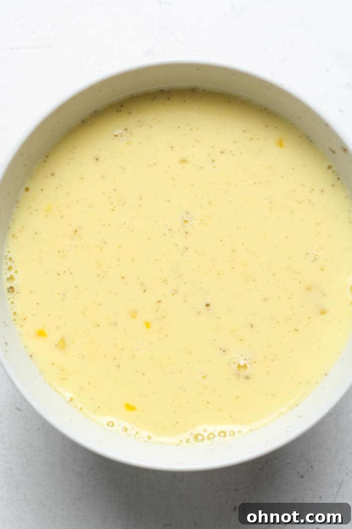 Egg mixture in a bowl, with milk, salt, and pepper added, ready for a final whisk before pouring into the crust.