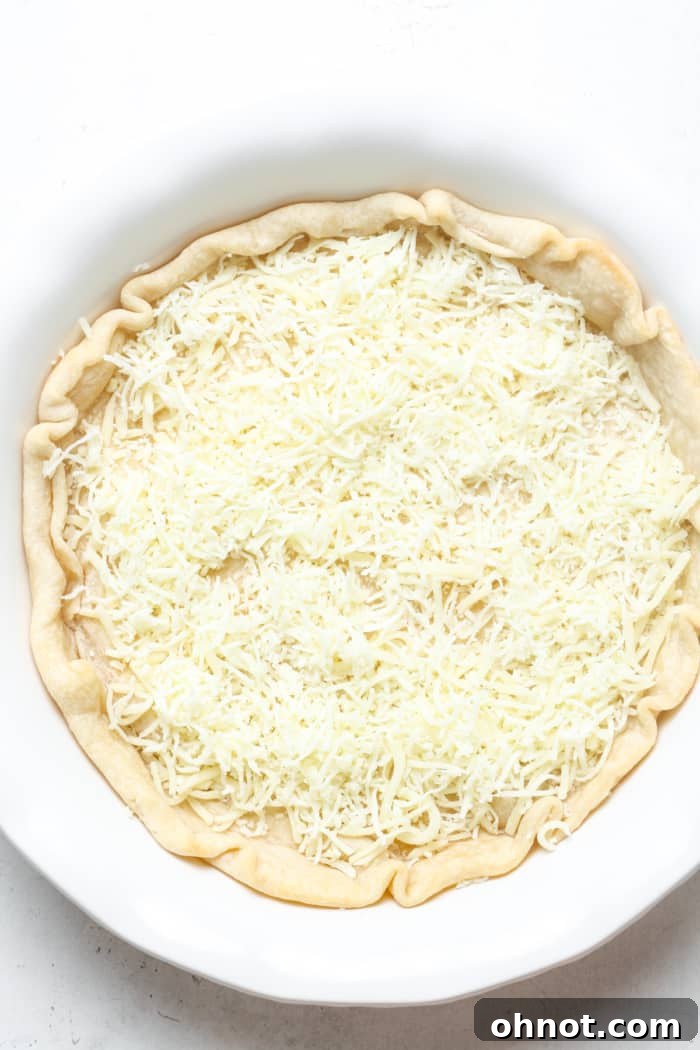 Pie crust with a generous layer of shredded Gruyere cheese spread evenly across the bottom.