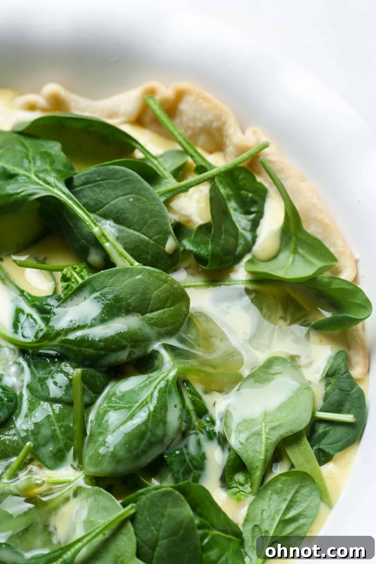 Quiche filling, a creamy egg and spinach mixture, being poured into the pie crust with cheese.