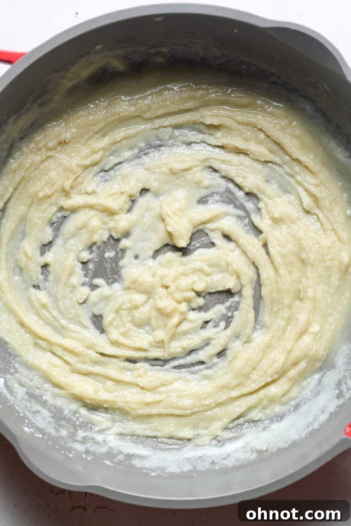 Flour being whisked into melted butter in a skillet to form a smooth roux.
