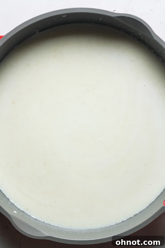 Whole milk being poured into the roux in a skillet, ready to be stirred for the cheese sauce base.
