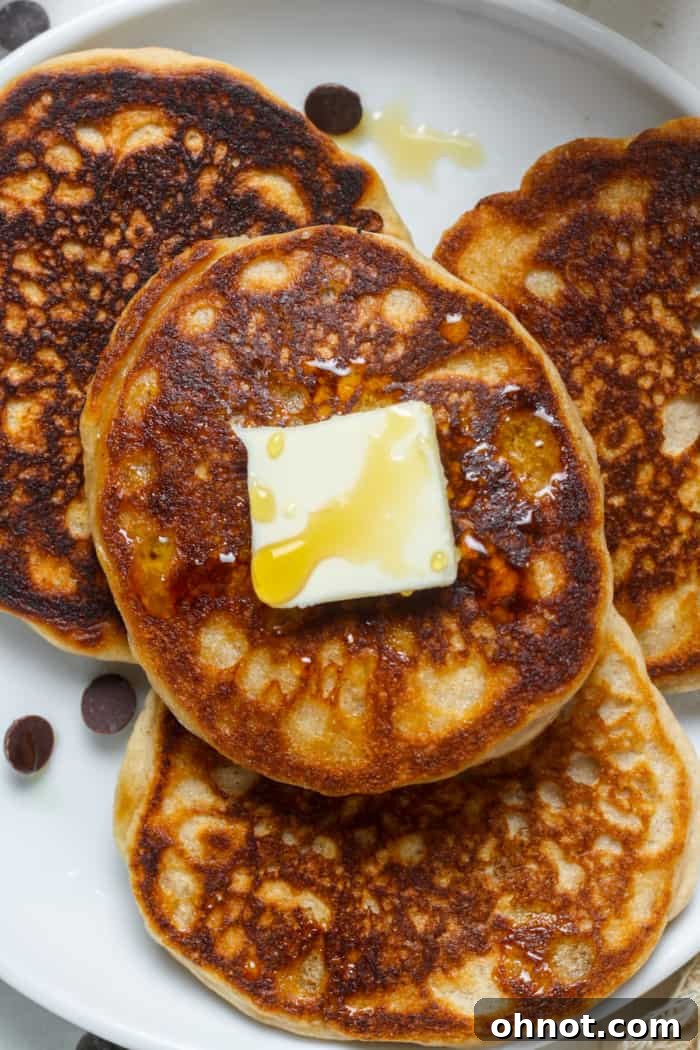 A stack of golden brown sourdough pancakes on a plate, topped with fresh berries and maple syrup, with a cup of coffee in the background.