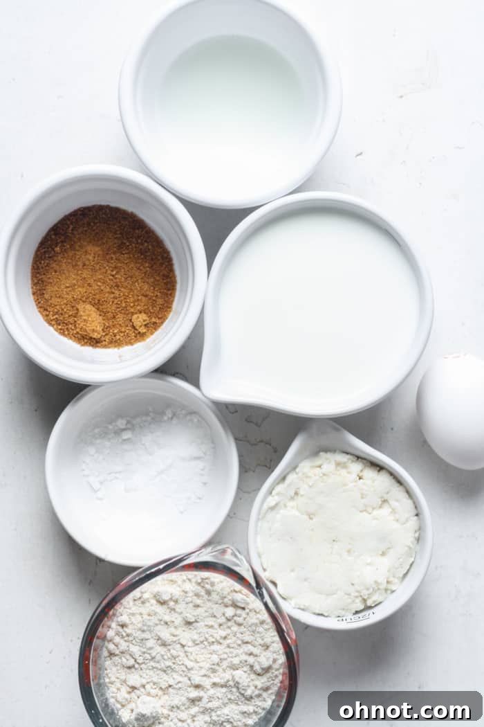Various ingredients for sourdough pancakes laid out on a wooden surface: flour, milk, eggs, sourdough starter, oil, sugar, and baking powder.