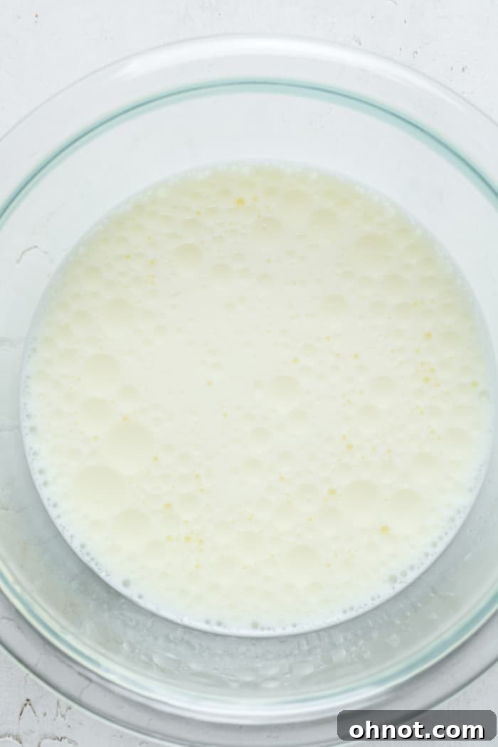 Milk and eggs being whisked together in a glass mixing bowl.