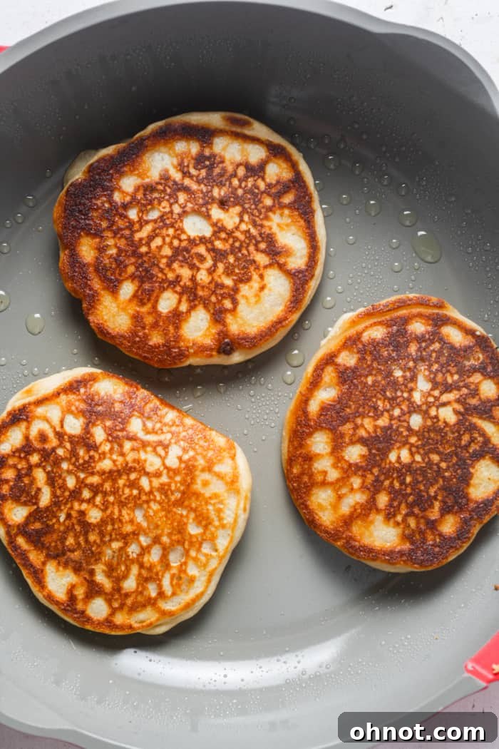 A golden-brown sourdough pancake cooking on a skillet, showing a perfectly cooked side.