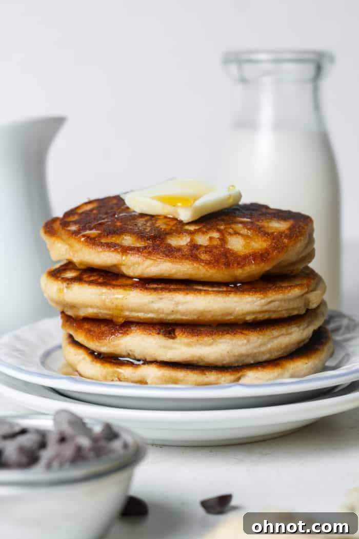 A tall stack of fluffy sourdough pancakes on a white plate, ready to be served, with a hint of toppings in the background.