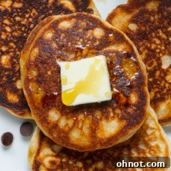 A stack of golden brown sourdough pancakes on a plate, topped with fresh berries and maple syrup.