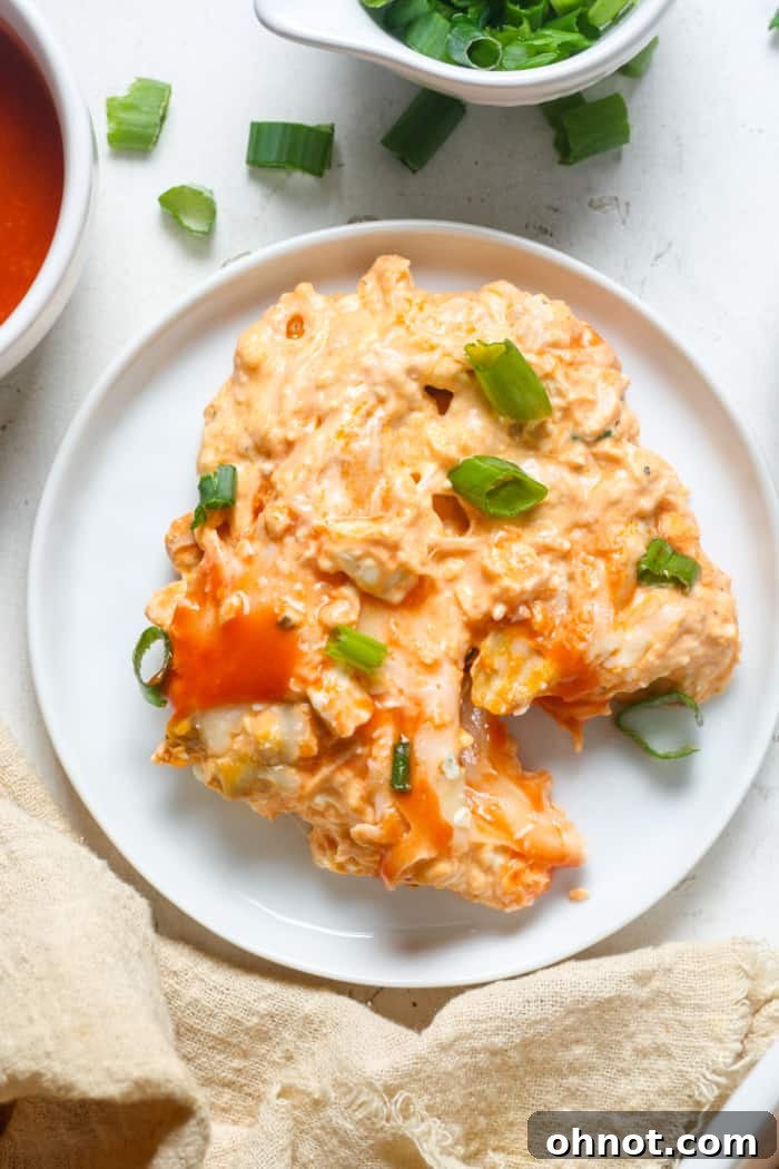 A generous serving of keto buffalo chicken dip on a plate, garnished with fresh green onions and ready to be enjoyed with dippers.