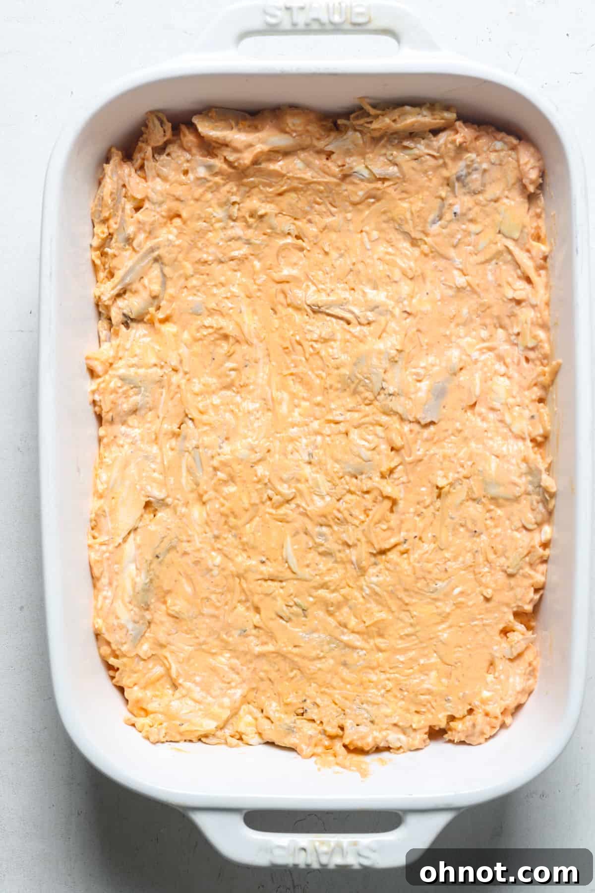 A baking pan filled with the creamy chicken mixture, smoothed out and ready for toppings.