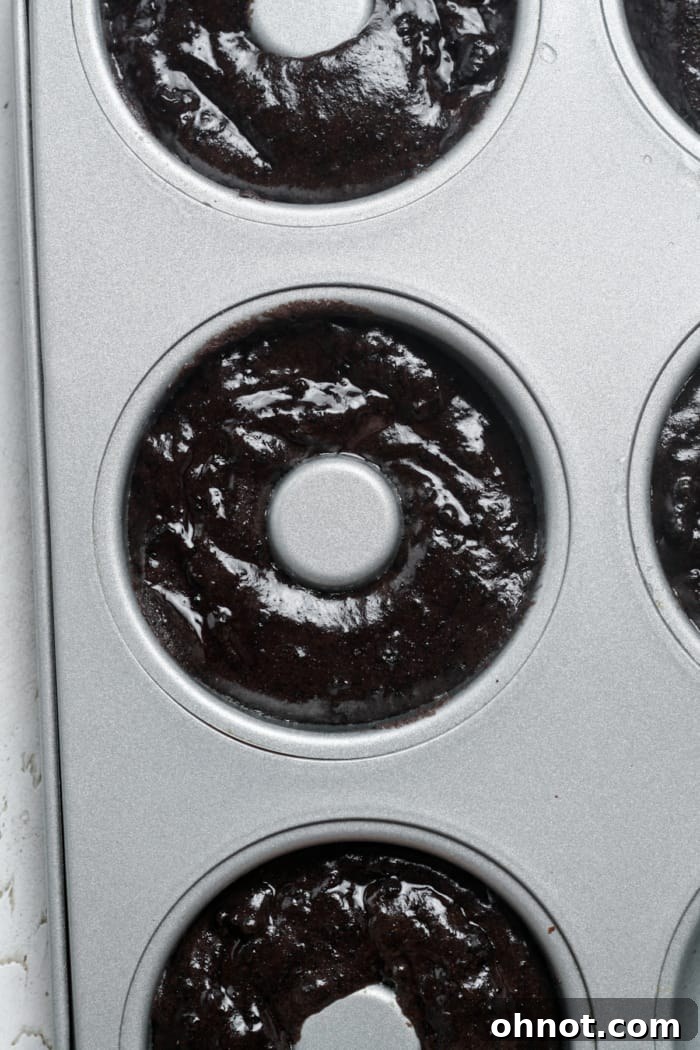 Donut pan with cavities partially filled with chocolate Oreo batter, ready for the oven.