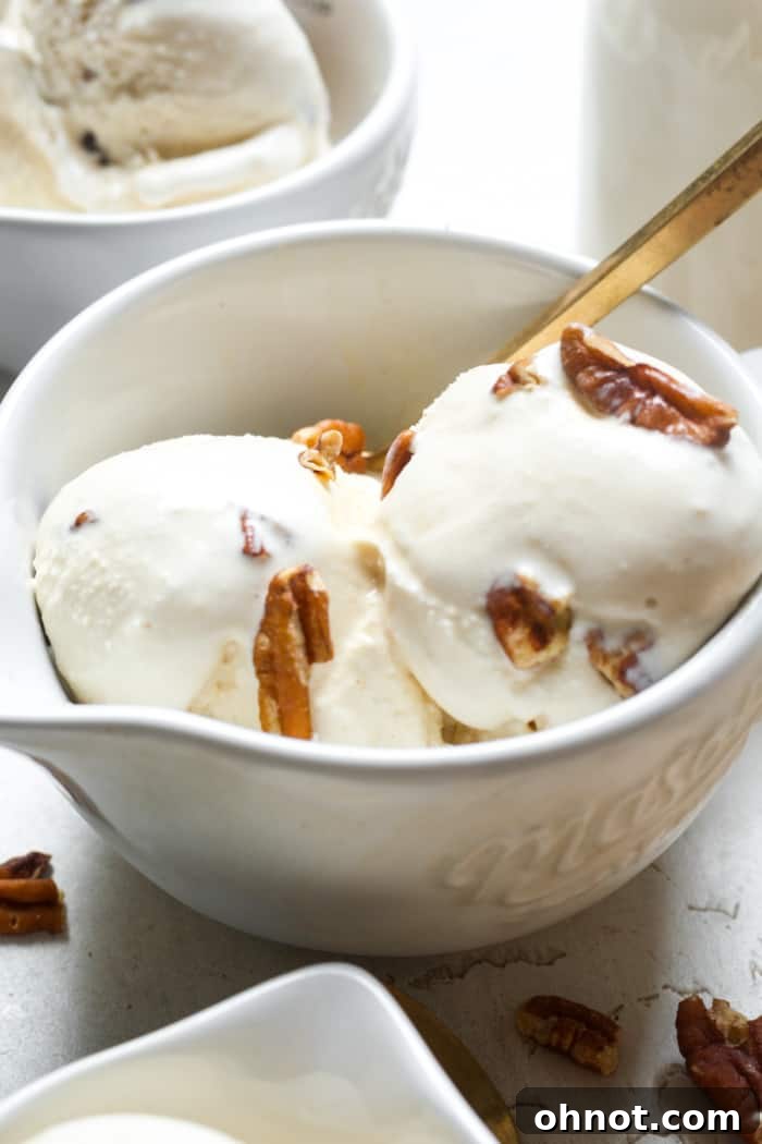 A scoop of homemade butter pecan ice cream with whole pecans on top in a white bowl.